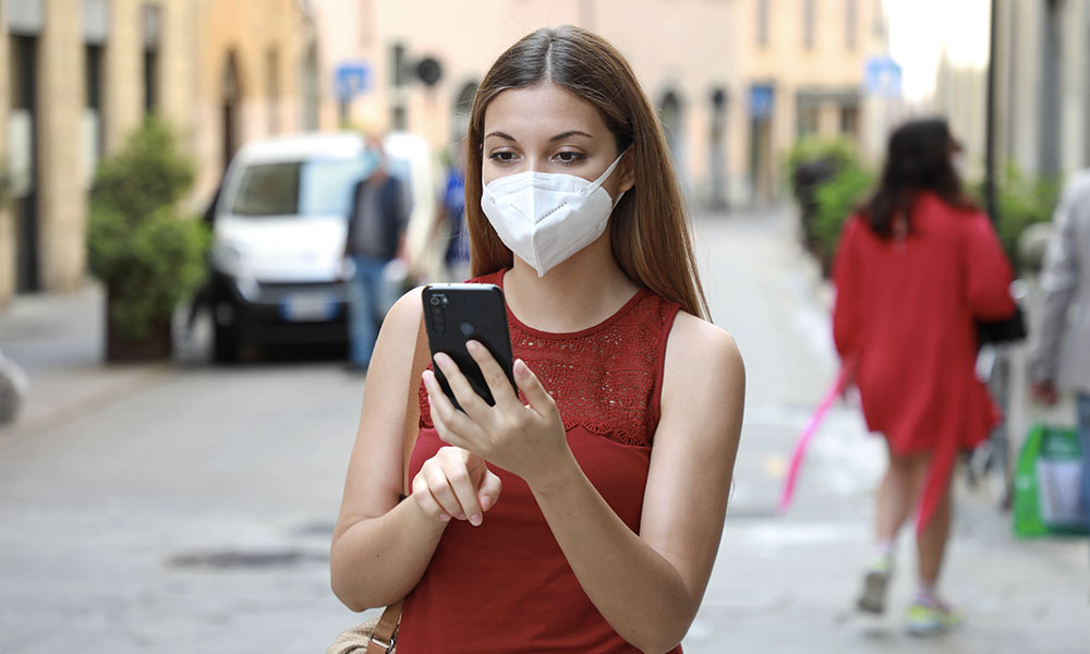 Woman in red on street wearing mask using iPhone